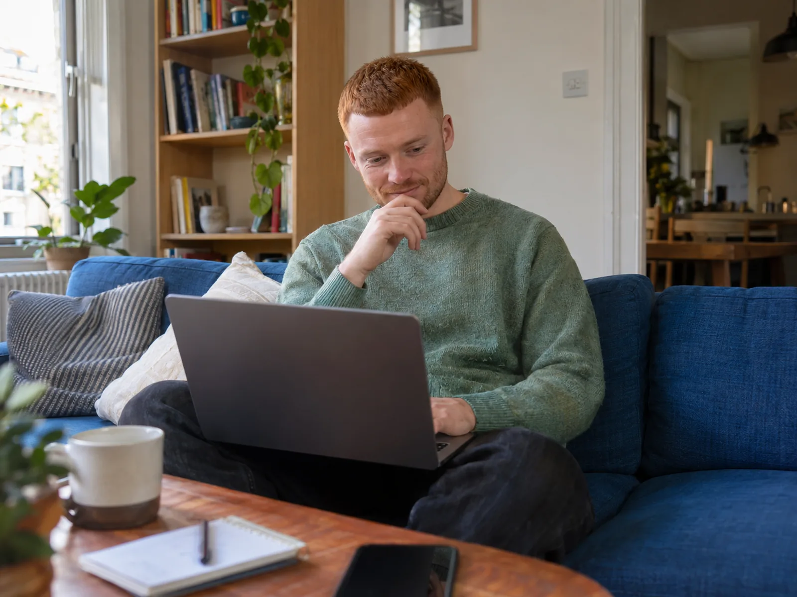 Young man with a ginger buzz cut using a laptop on a blue sofa at home