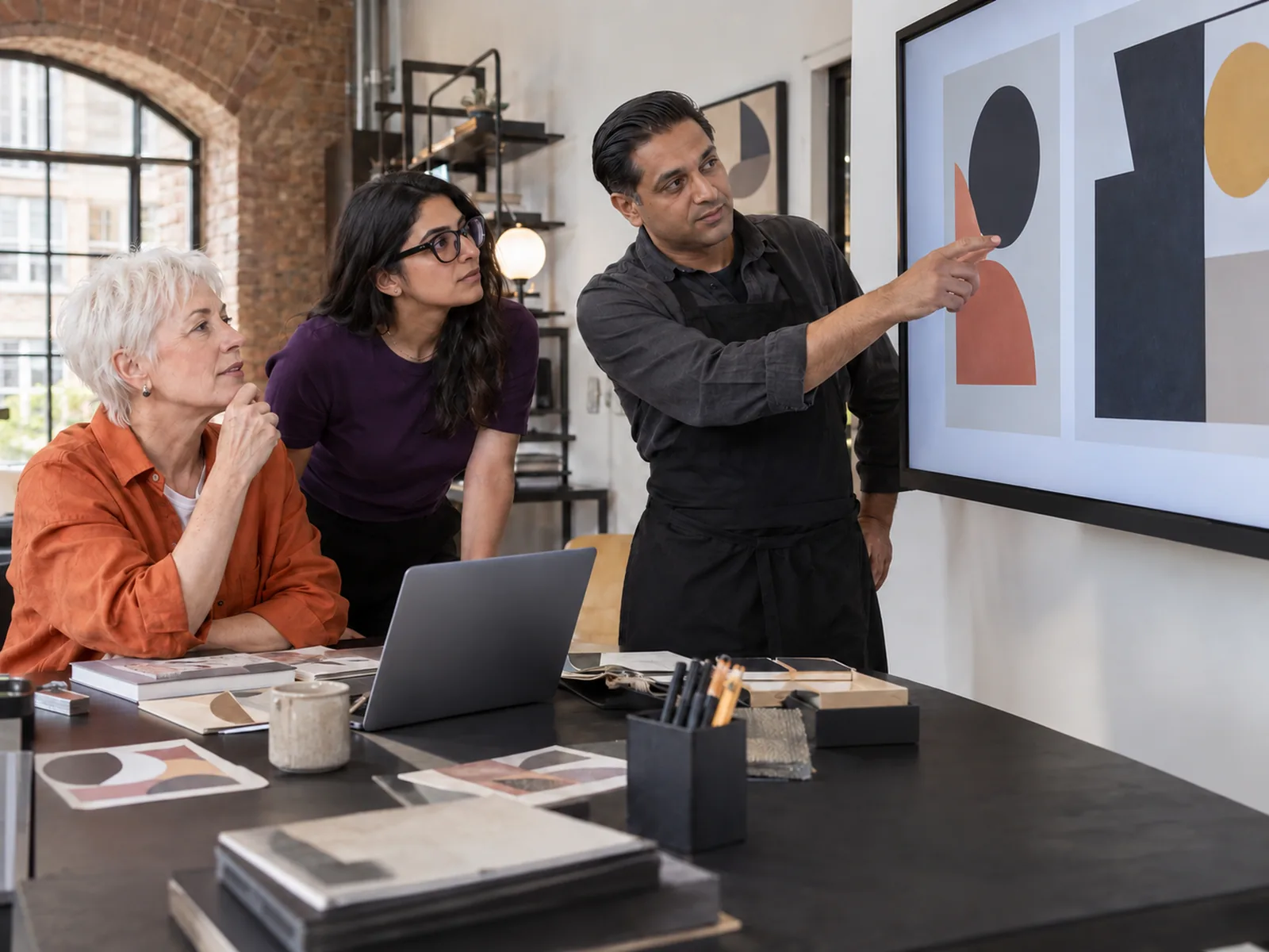Three colleagues looking at abstract designs on a wall screen in a studio with a brick arch