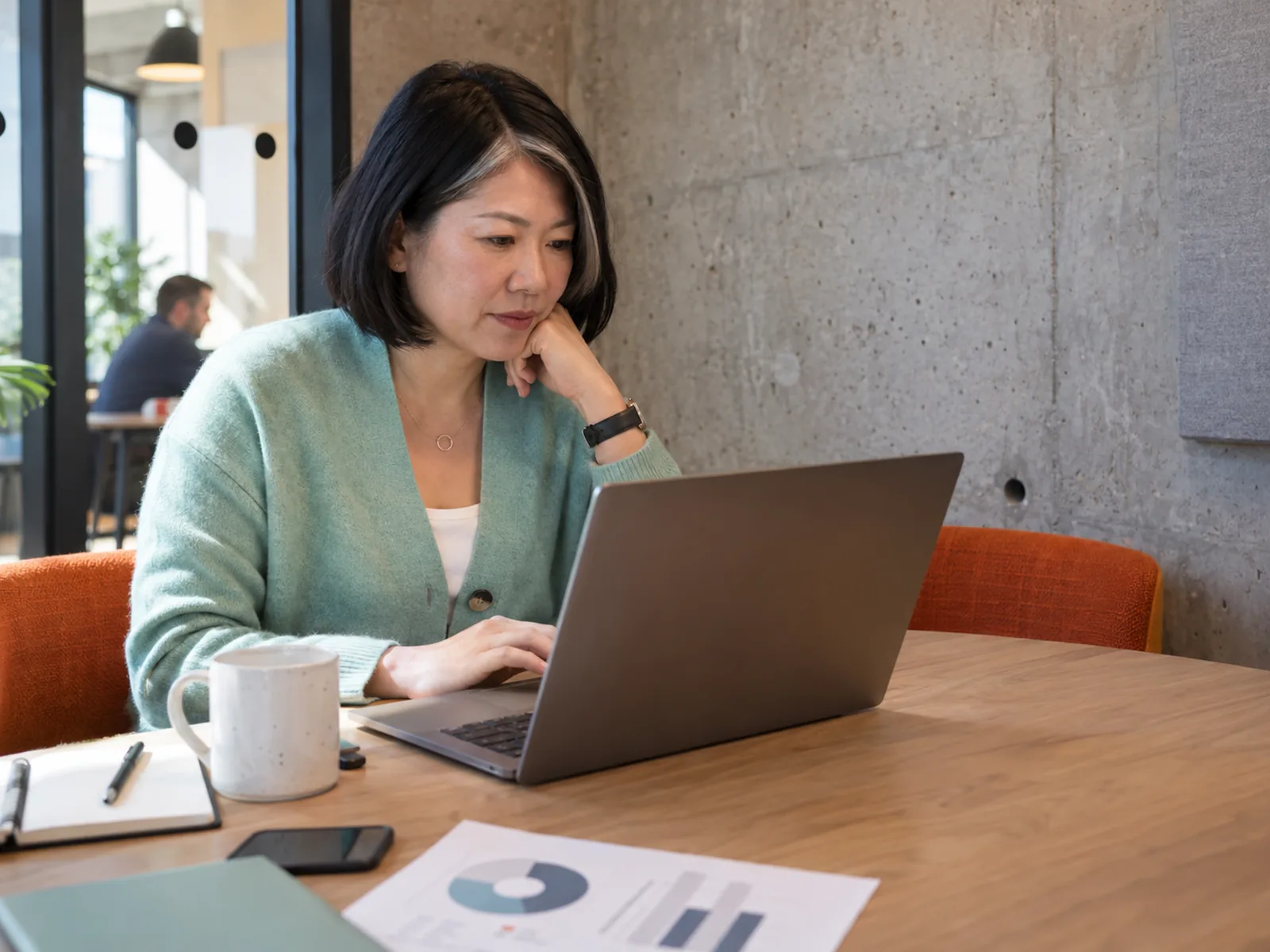Woman with a black bob and silver streak reading a laptop in a co-working booth
